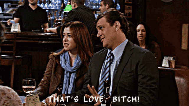 a man and a woman are sitting at a table in a bar and the man says that 's love bitch