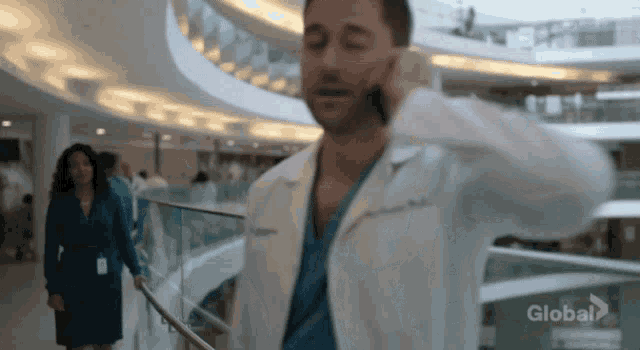 a man in a lab coat is talking on a cell phone while walking down a hospital hallway .