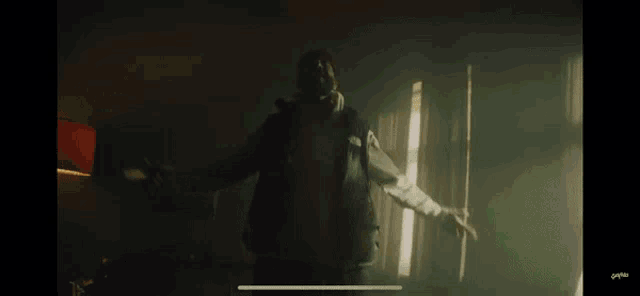 a man in a hooded jacket is standing in a dark room with smoke coming out of the windows .