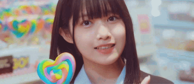 a girl in a school uniform is holding a heart shaped lollipop in her hand .