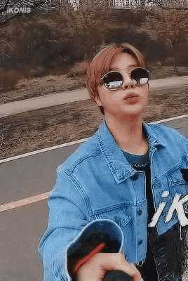 a man wearing sunglasses and a denim jacket is taking a selfie .