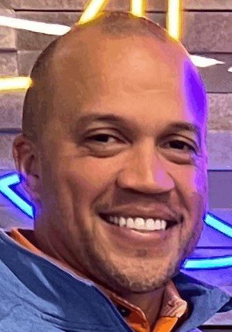 a close up of a man 's face with a beard smiling in front of a neon sign .