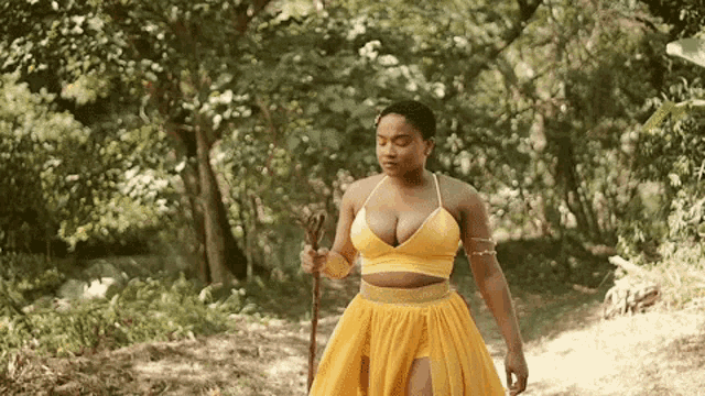 a woman in a yellow dress is walking through a forest holding a cane .