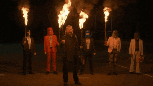 a group of men in suits and masks are holding flaming torches in their hands
