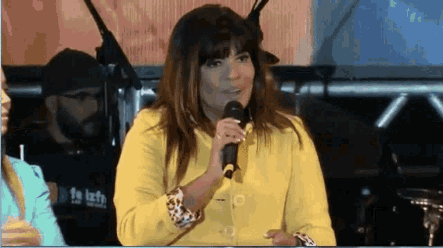 a woman in a yellow jacket is singing into a microphone while a man in a black shirt stands behind her