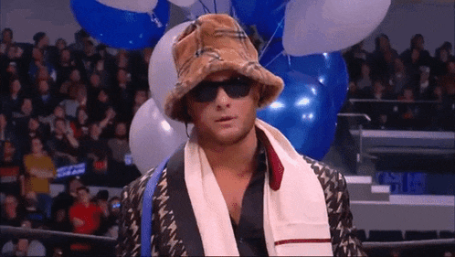 a man wearing a hat and sunglasses is standing in front of balloons in a stadium .