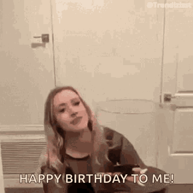 a woman is sitting in front of a door holding a glass of wine and saying happy birthday to me .