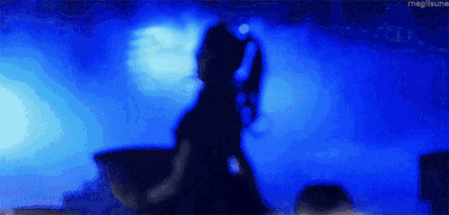 a silhouette of a person standing in a dark room with a blue light behind them .