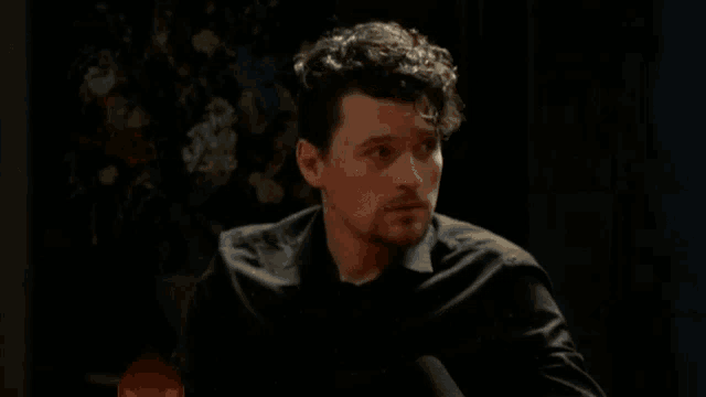 a man with curly hair wearing a black shirt looks at the camera