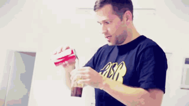a man wearing a black shirt with the word absa on it is pouring a drink into a glass .