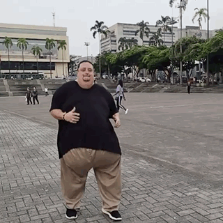 a man in a black shirt and khaki pants is standing on a brick sidewalk and giving a thumbs up