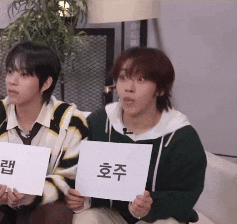 two young men are sitting on a couch holding signs with asian writing on them
