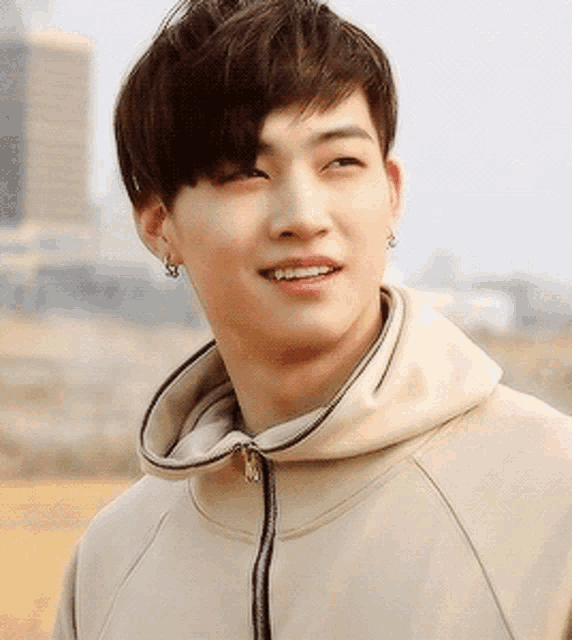 a young man wearing a tan hoodie and earrings smiles