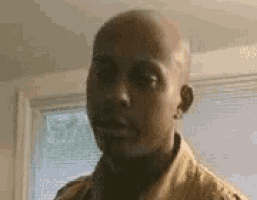 a man with a bald head is standing in front of a window in a room .