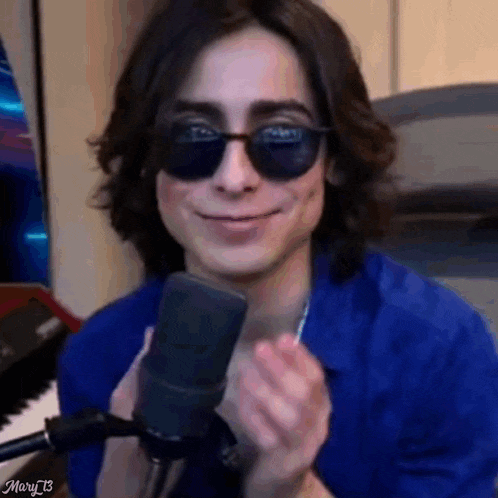 a young man wearing sunglasses is standing in front of a microphone and smiling .