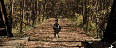 a boy walking down a path in the woods with a backpack