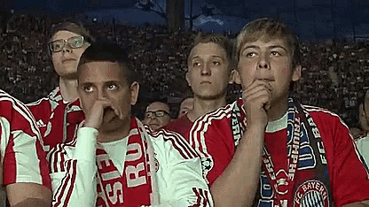 a group of young men are watching a soccer game and one of them has a scarf around his neck that says bayern