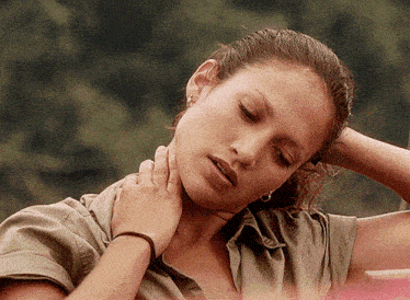 a woman holds her hand to her neck and looks down