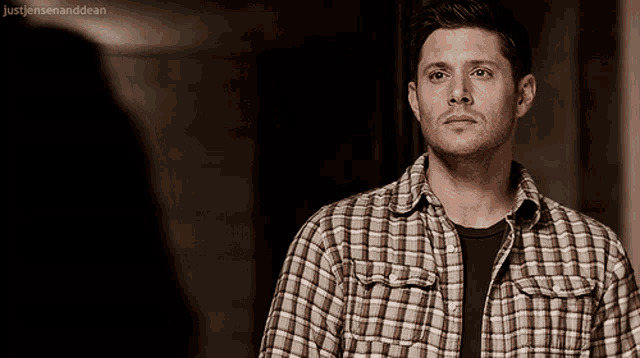 a man in a plaid shirt is standing in a dark room with justjensenanddean written below him