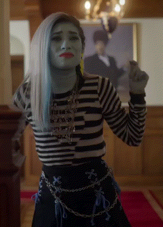 a woman with blue hair and a striped shirt is standing in front of a picture of a man .