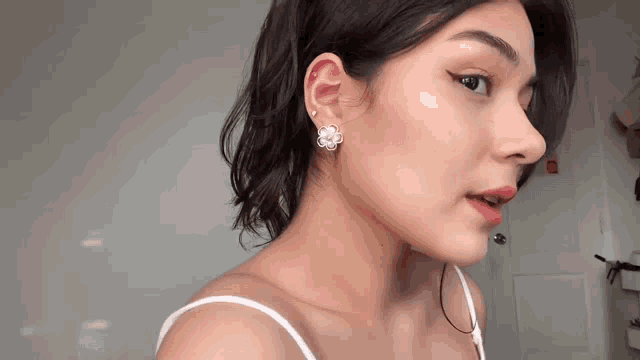 a close up of a woman 's face wearing earrings and a white tank top .