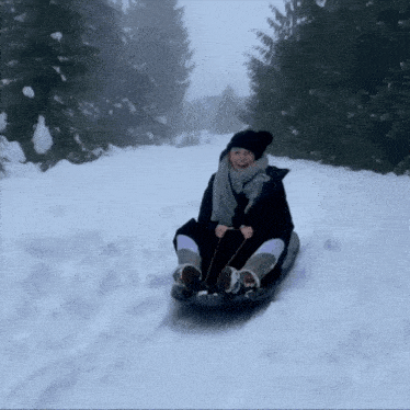 a woman sledding down a snowy hill with trees in the background