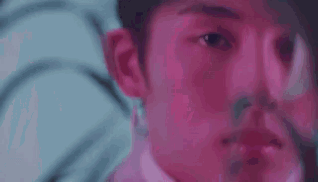 a close up of a young man 's face in a pink and blue light .