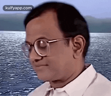 a man wearing glasses and a white shirt is looking at the water .