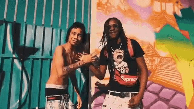 a couple of men are standing next to each other in front of a graffiti wall .