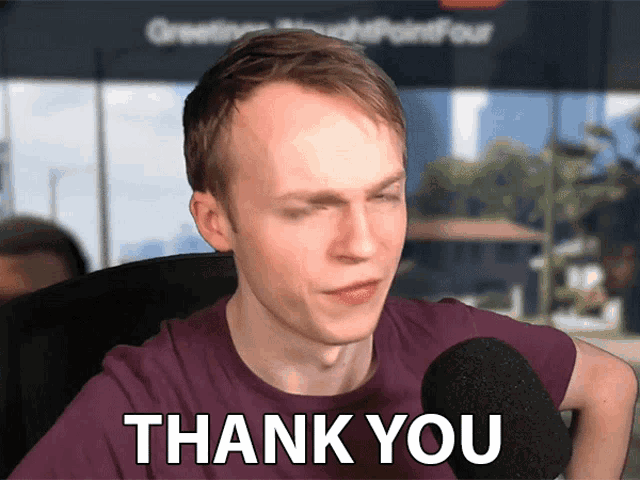 a man wearing a purple shirt says thank you in front of a microphone