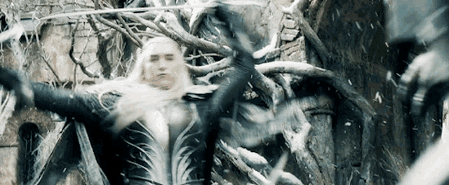 a man with long white hair is standing in front of a tree with a sword in his hand .