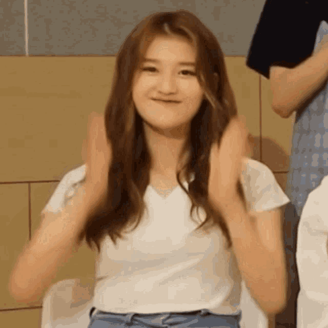 a woman in a white shirt is clapping her hands while sitting on a chair .