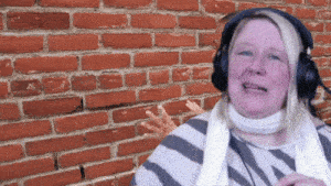 a woman wearing headphones stands in front of a red brick wall