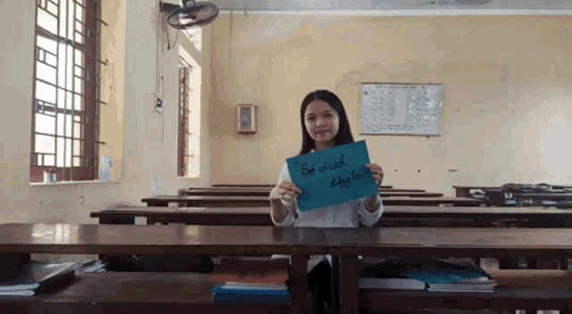 a girl in a classroom holds up a sign that says se co cach
