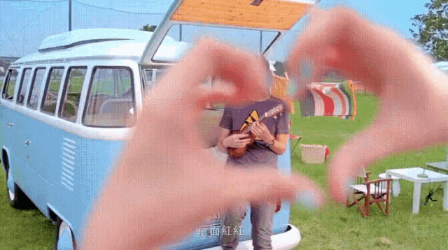 a person making a heart shape with their hands in front of a blue bus