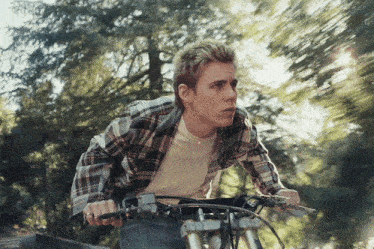 a man in a plaid shirt is riding a bike on a road