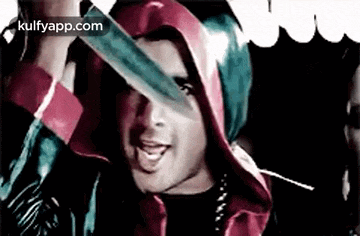a man in a red hooded jacket is holding a large knife in front of his face .