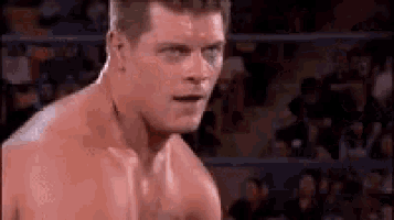 a shirtless wrestler is standing in a ring with his mouth open .