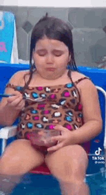 a little girl is sitting in a chair in a pool eating ice cream .