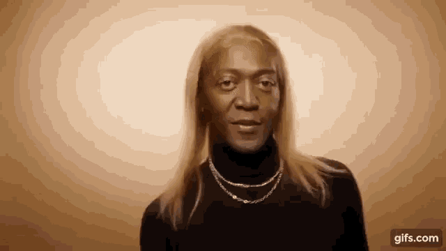 a woman with long blonde hair is wearing a black turtleneck and a gold necklace .