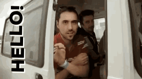 a man in a red shirt is standing in the doorway of a white van and says hello .