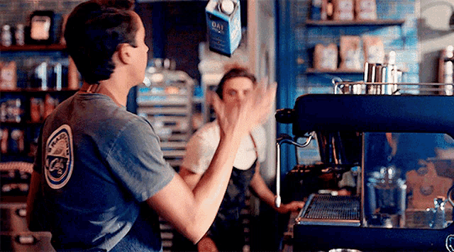 a man standing in front of a coffee machine giving a high five to a woman