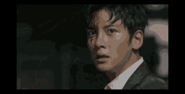 a man with blood on his face is wearing a suit and white shirt .
