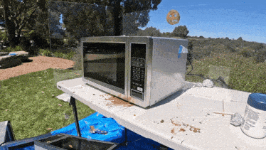 a silver microwave sits on a messy table with a smiley face on the window