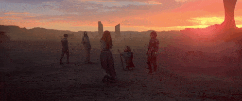 a group of people standing in a desert with a sunset in the background