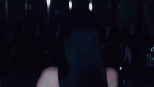 a woman in a black dress is dancing in front of a crowd of people