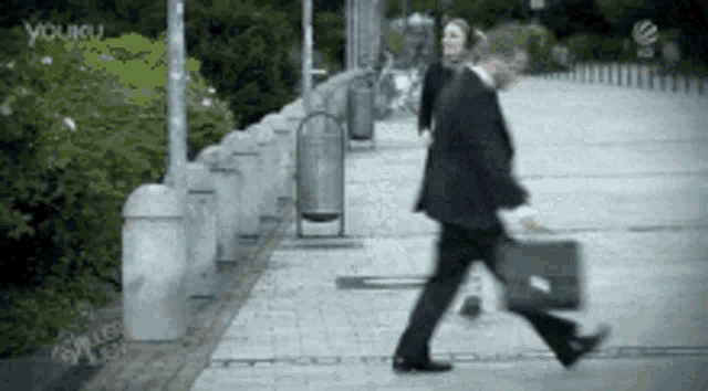 a man in a suit is walking down a sidewalk with a green briefcase