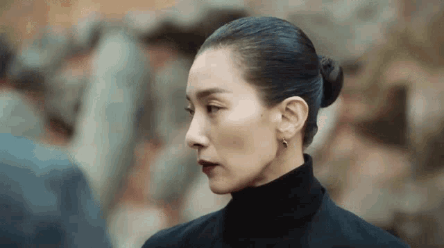 a woman in a black turtleneck and earrings is standing in front of a crowd .