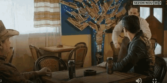 a man in a cowboy hat sits at a table with a can of bud light on it