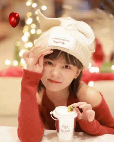a girl wearing a white hat and a red sweater is sitting at a table with a cup of coffee in front of her